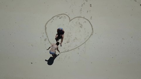 A drone shot of a couple drawing a heart on the white sand beach on a small island near Maumere, Indonesia. Happy and careless moments. Waves gently washing the shore. Romance and love. Happiness
