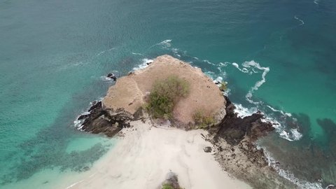 A top-down drone shot of an idyllic Koka Beach. Hidden gem of Flores, Indonesia. Headland going straight into the open sea. Beauty in the nature. Calm waves washing the cliff's slopes. Serenity. 

