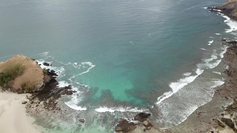 A drone shot of an idyllic Koka Beach. Hidden gem of Flores, Indonesia. A headland going straight into the open sea. A small settlement at the beach. Few boulders popping out from the sea. Serenity
