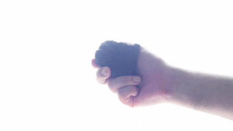 Male hand with a piece of coal in bright light on a light background.