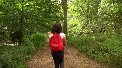 Teenage African American mixed race  girl young woman hiking with red backpack and taking photographs with a camera in forest woodland