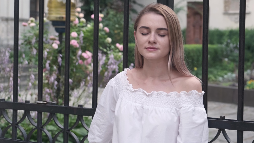 Portrait of a young attractive blonde girl in a white dress looking at the camera, smiling, urban background. Attractive girl standing in city street. Luxury fashion woman in dress posing.