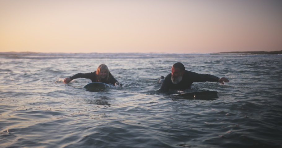 Senior man and woman surfing in the water at sunset Royalty-Free Stock Footage #1056480128