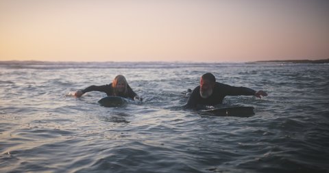 Senior man and woman surfing in the water at sunset