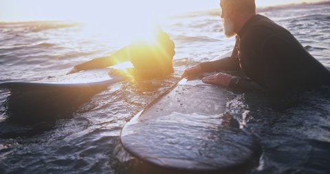 Senior man and woman surfing in the water at sunset