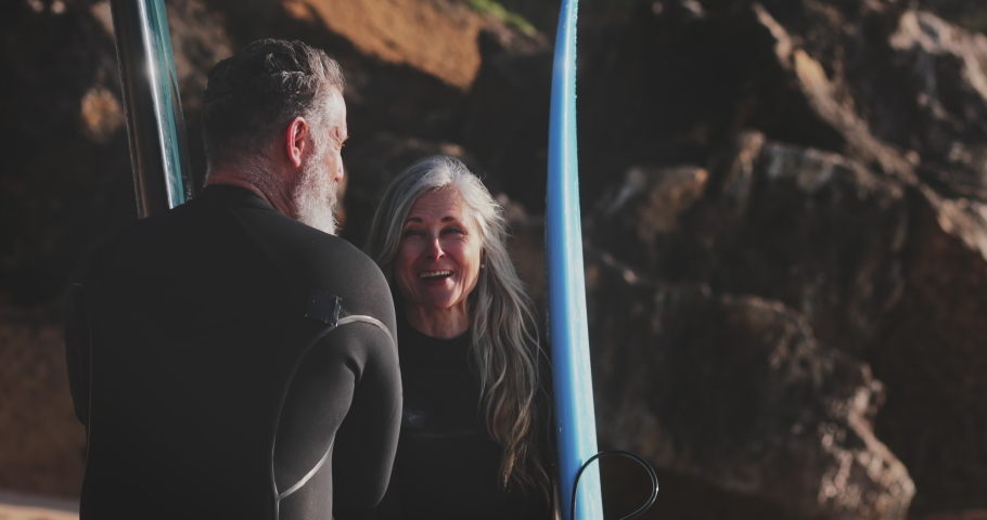 Close-up senior man and woman holding up surfboards at beach | Shutterstock HD Video #1056480197