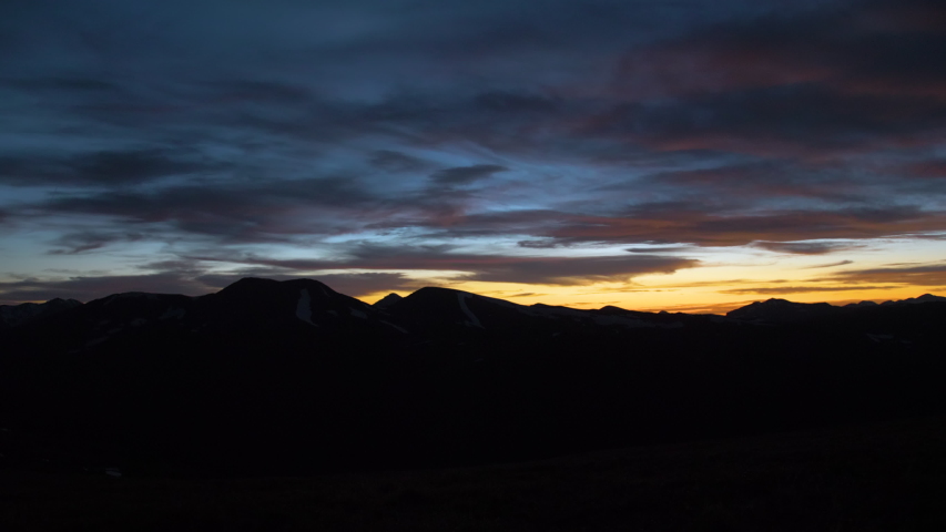 Pan movement looking over dark mountain range with colorful sunset sunrise in cloudscape