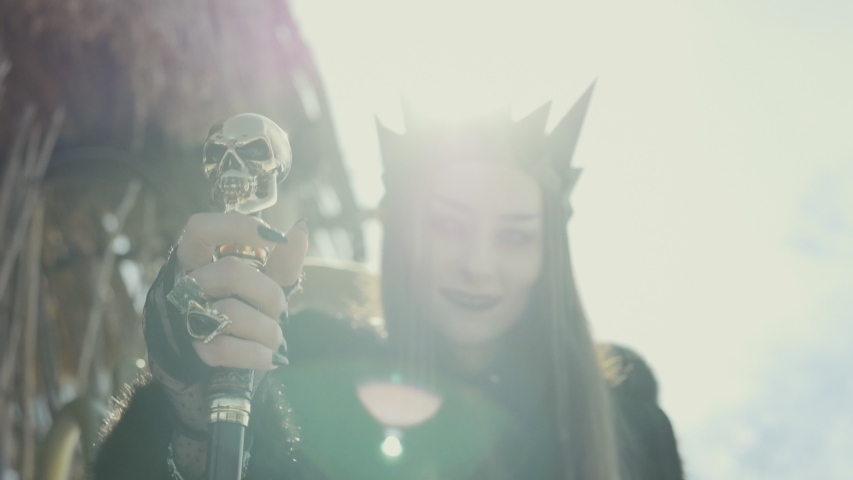 Close up of a witch with a black crown on her head and a staff in her hands