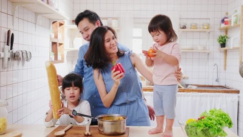 Family relationship, Asian happy family dancing in kitchen room at house. Father mother and children having fun making food together. Little baby standing on counter and sister playing with bread.