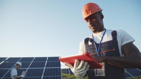 Black energy specialist using digital tablet reading information to check the efficiency of solar panel construction. Green energy jobs. Technology. Innovation.