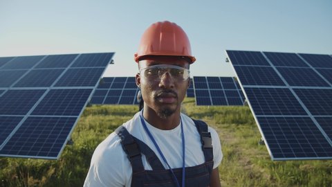 Portrait of afro-american ecology worker in hard hat standing at solar panel field. Industrial people. Sustainable energy. Technology.