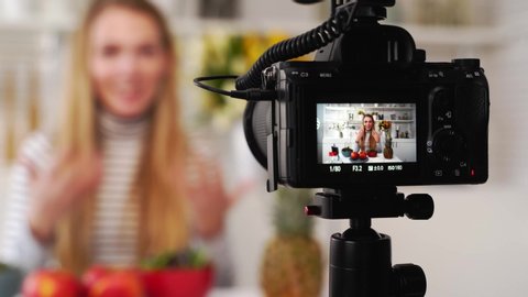 Camera screen recording - focus transition - Food blogger cooking fresh vegan salad of fruits in kitchen studio, filming tutorial. Female influencer holds apple, pineapple, talks about healthy eating.