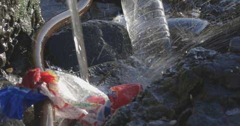 Water splashes into a polluted drainage catchment area of plastic littered debris.
