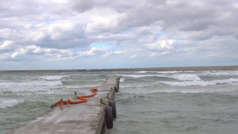Pier with a wave on the gray background of the sea with a pier, a path to the sea in the summer during the sea, storm
