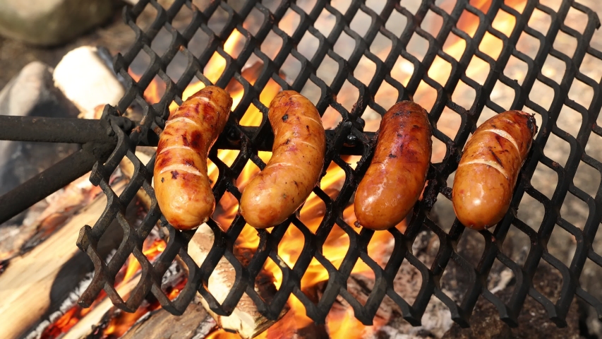 Grilling sausages on barbecue grill outdoor. Smoke and fire. Close up.