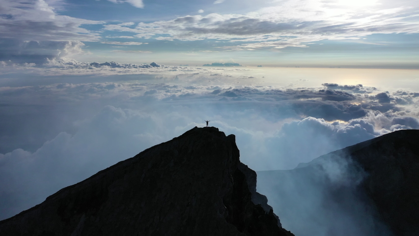 Climbing a volcano. Higher than clouds. 4k video. A man walks along the high mountains. Vulcano agung. a man stands on the edge of a crater. Eruption. Batur and abang in Kintmani. hands up | Shutterstock HD Video #1056496628