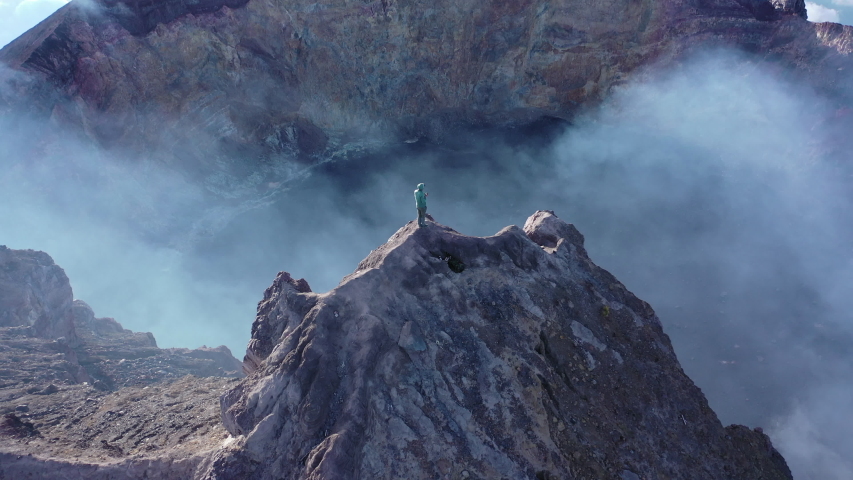 Climbing a volcano. Higher than clouds. 4k video. A man walks along the high mountains. Vulcano agung. a man stands on the edge of a crater. Eruption | Shutterstock HD Video #1056496631