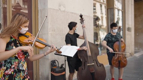 trio strings musical band wearing protective masks playing music outside in the street in pedestrian zone in pandemic time