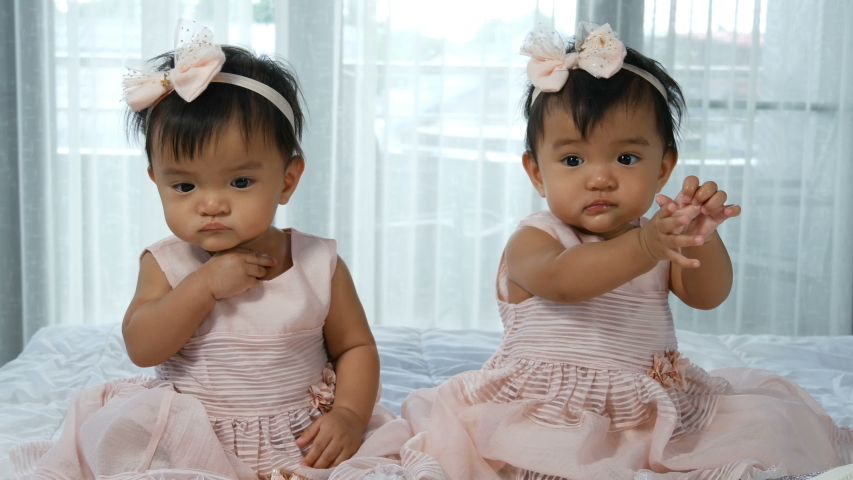 two twin babies in pink dress on a bed