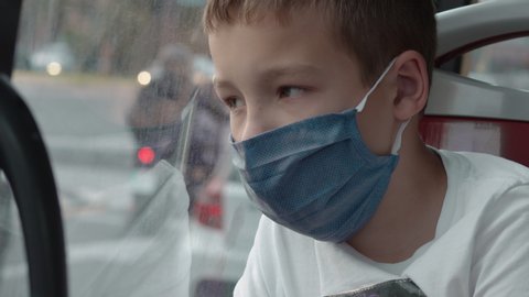 Close-up shot of a kid being bored and tired with bus ride and wearing face mask. Living with Covid-19 precautions and restrictions