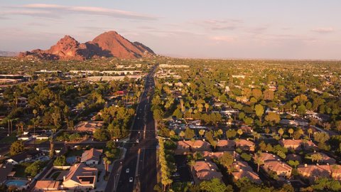 Aerial footage of Phoenix, Arizona  flying above Camelback Road and mountain glowing red in the evening sun.   