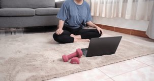 Home Workout of Young asian woman watching practice video online training yoga instructor modern laptop computer meditate posture relax breathe easy seat pose gym healthy lifestyle at home.