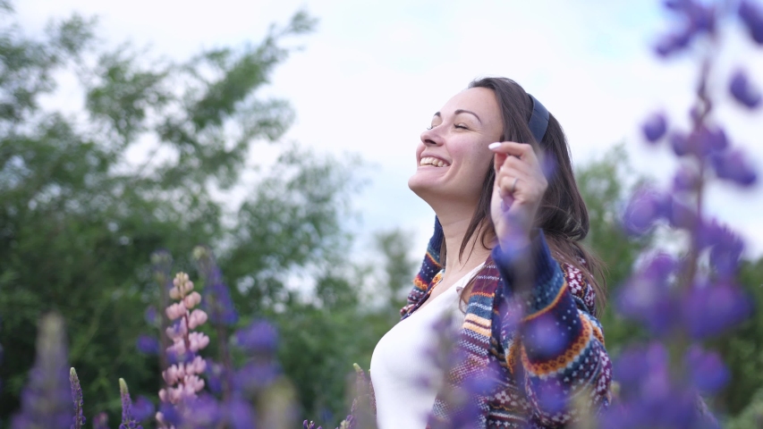 Pretty young happy woman in headphones dancing in a field of flowers lupins.