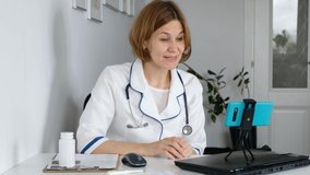 Woman doctor wear uniform with stethoscope talk by conference video call or doing webinar on smartphone, distant medical consultation in internet