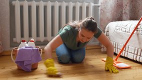 A woman rubs the wooden floor with a brush. The cleaning lady cleans up the house 4k video.