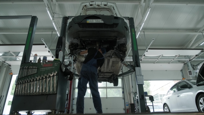 Auto mechanic working underneath car lifting machine at the garage. Auto repair shop, Car service, repair.     Royalty-Free Stock Footage #1056508877