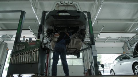 Auto mechanic working underneath car lifting machine at the garage. Auto repair shop, Car service, repair.    
