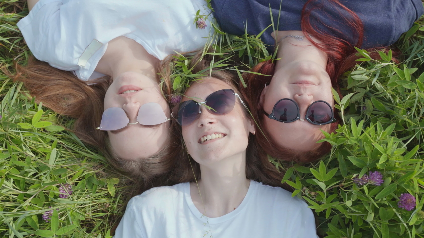 Three friendly girlfriends are lying on the grass with sunglasses and chewing gum.