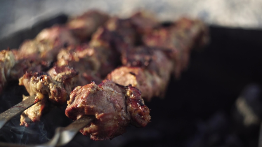 Shashlik or shashlyk preparing on a barbecue grill over charcoal. Grilled cubes of pork meat on metal skewer. Meat on skewers is roasted on fire Royalty-Free Stock Footage #1056511667