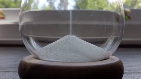 Close up of sand falling into a pile inside an hour glass timer on a desk