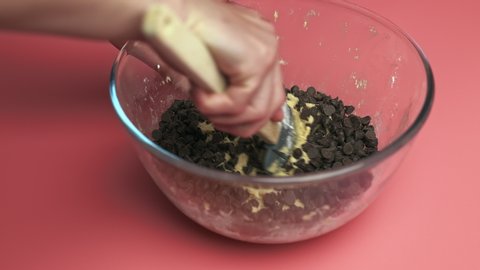 Adding Chocolate Chips into a bowl with liquid Chocolate Chip Cookies dough in 4K. Concept of making Cookies dough in slow motion.
