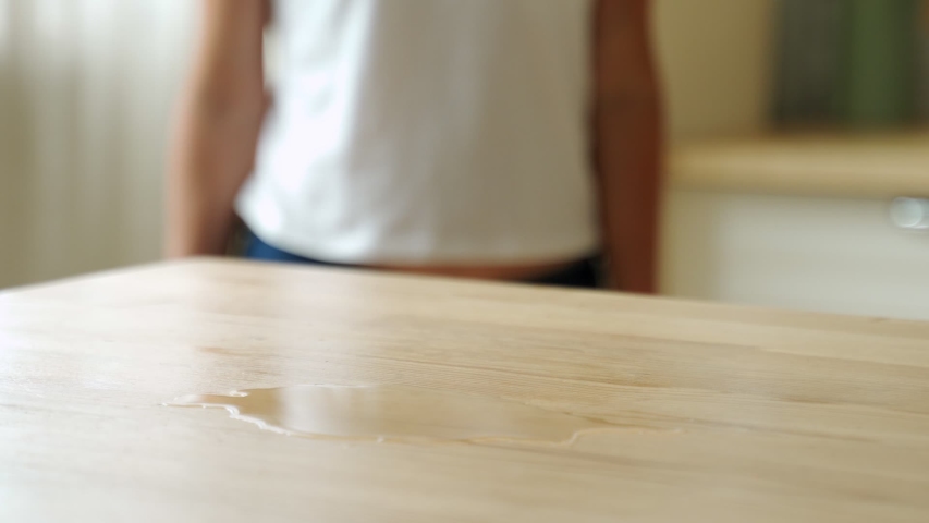 Housewife wiping spilled coffee or tea from a wooden kitchen table. Female using a household cleaner wipe for cleaning.