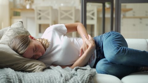 Woman suffering from stomachache lying down on sofa