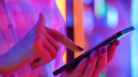 Woman using smartphone device at interactive exhibition or museum with purple illumination - scrolling and touching - close up side view. Futuristic, retrowave, immersive, entertainment concept