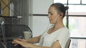 Portrait of beautiful young woman with earphones working on laptop while sitting at home office