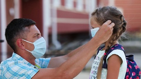 The father puts a surgical  masks on his daughter is face. A little girl is going to school during the quarantine period. Concept of coronavirus COVID-19. 