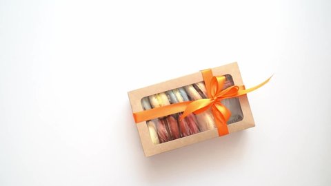 pack box with ribbon and inside macarons enters the frame on a white background. slow motion