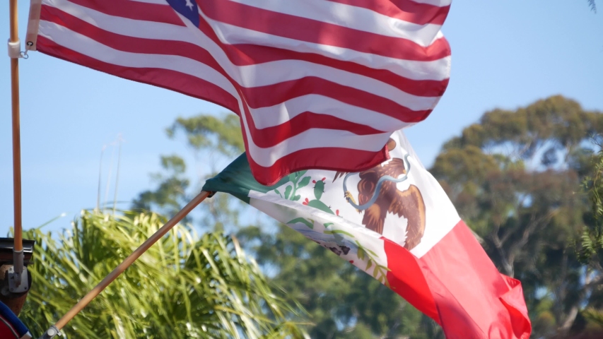 Mexican tricolor and American flag waving on wind. Two national icons of Mexico and United States against sky, San Diego, California, USA. Political symbol of border, relationship and togetherness. Royalty-Free Stock Footage #1056525962