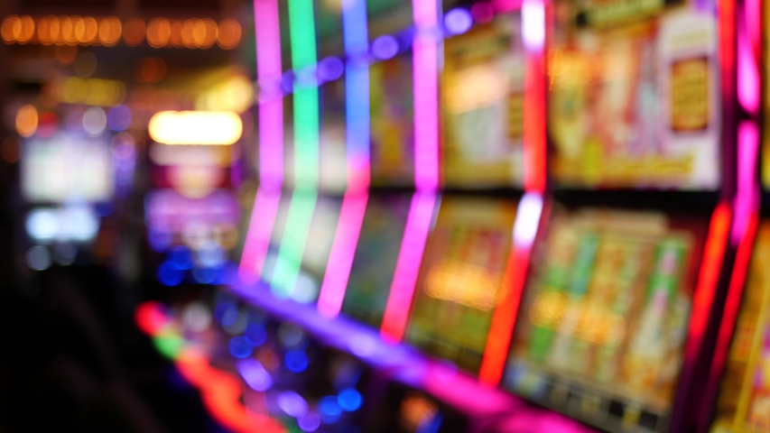 Defocused slot machines glow in casino on fabulous Las Vegas Strip, USA. Blurred gambling jackpot slots in hotel near Fremont street. Illuminated neon fruit machine for risk money playing and betting. Royalty-Free Stock Footage #1056526037