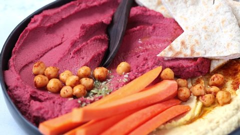 Beetroot hummus and classic hummus in black dish with carrots and pita bread. Plant based diet concept.