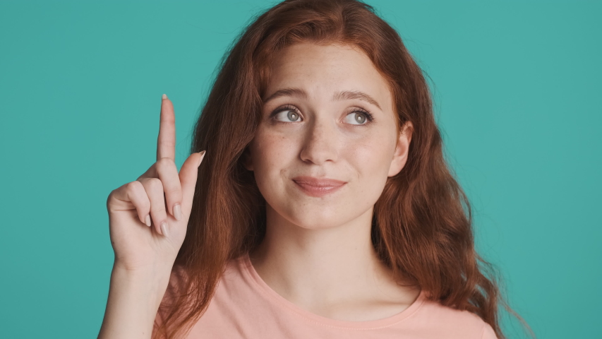 Portrait of beautiful thoughtful redhead woman biting her lip and showing new idea gesture over colorful background | Shutterstock HD Video #1056532193