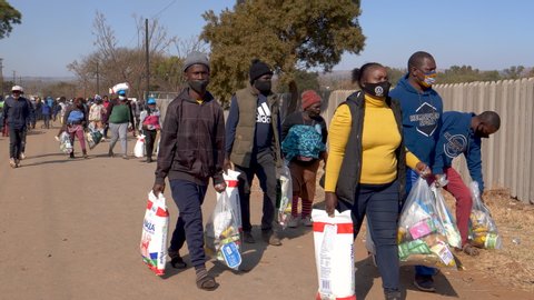 AFRICA,SOUTH AFRICA,CIRCA 2020. Poor and unemployed people walking back to their informal settlement with food parcels they received from the NGO, The Gift of the Givers, during the Covid-19 pandemic