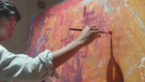 Asian Male Artist Works On Abstract Painting, Moving Paint Brush Energetically He Creates Modern Masterpiece

