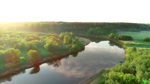 Aerial view of river and forest at summer sunny day, sky and clouds reflecting in water. Flying over sand river banks and green woodland. Sunrise on nature in beautiful place with natural landscape.