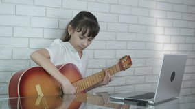Music lesson on video. A focused child learning to play the guitar from the internet video at home.