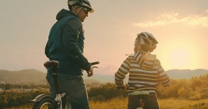 Father and son ride a bike. Happy cute boy in helmet learn to riding a bike in park on green meadow in summer day at sunset time. Family weekend. 4K video, Slow motion
